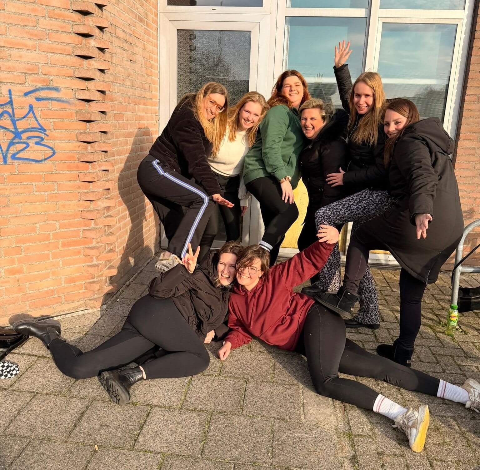 Een enthousiaste groep vrouwen poseert vrolijk buiten voor een karakteristieke stenen muur na een geslaagde workshop op locatie van YourMoves.